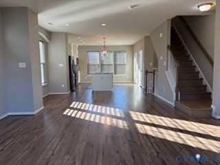 Open-concept interior featuring wood-finish flooring, recessed lighting, a central kitchen island, and a staircase with a white balustrade and wooden handrail