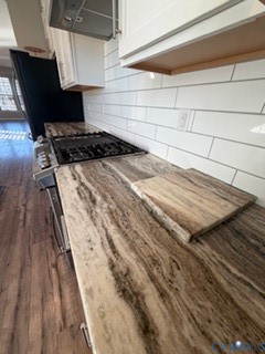 Natural stone countertops featuring organic veining, subway tile backsplash, white cabinetry, gas cooktop, and wood-finish flooring
