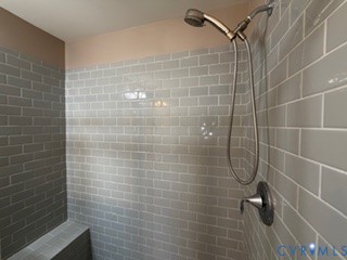 Shower enclosure featuring gray subway tile surround, built-in tiled bench, and adjustable handheld shower fixture with metallic finish