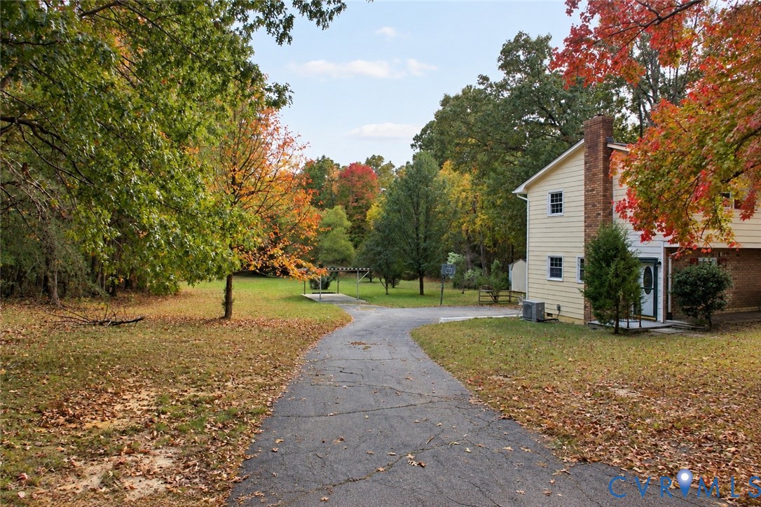 Two-story home with light-toned siding, exterior brick chimney, paved driveway, and expansive lawn featuring mature trees Two-story home with light-toned siding, exterior brick chimney, paved driveway, and expansive lawn featuring mature trees
