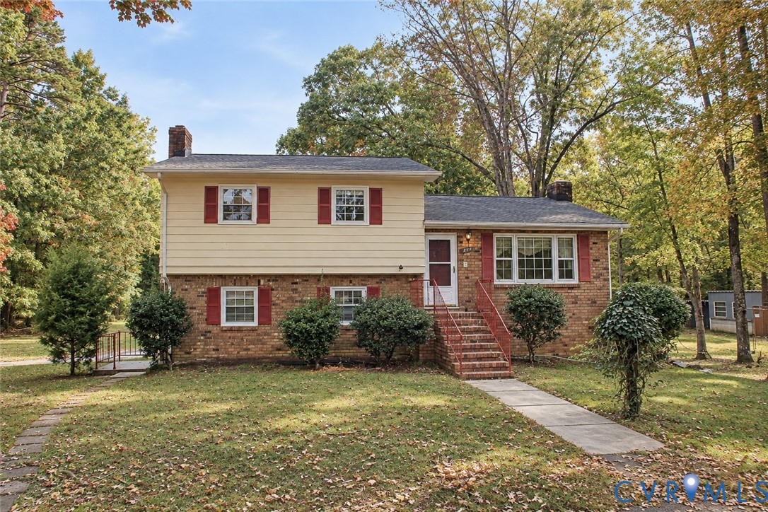 Split-level exterior featuring a brick and horizontal siding facade, red shutter accents, multi-pane windows, a brick-stepped entry, and a concrete walkway Split-level exterior featuring a brick and horizontal siding facade, red shutter accents, multi-pane windows, a brick-stepped entry, and a concrete walkway