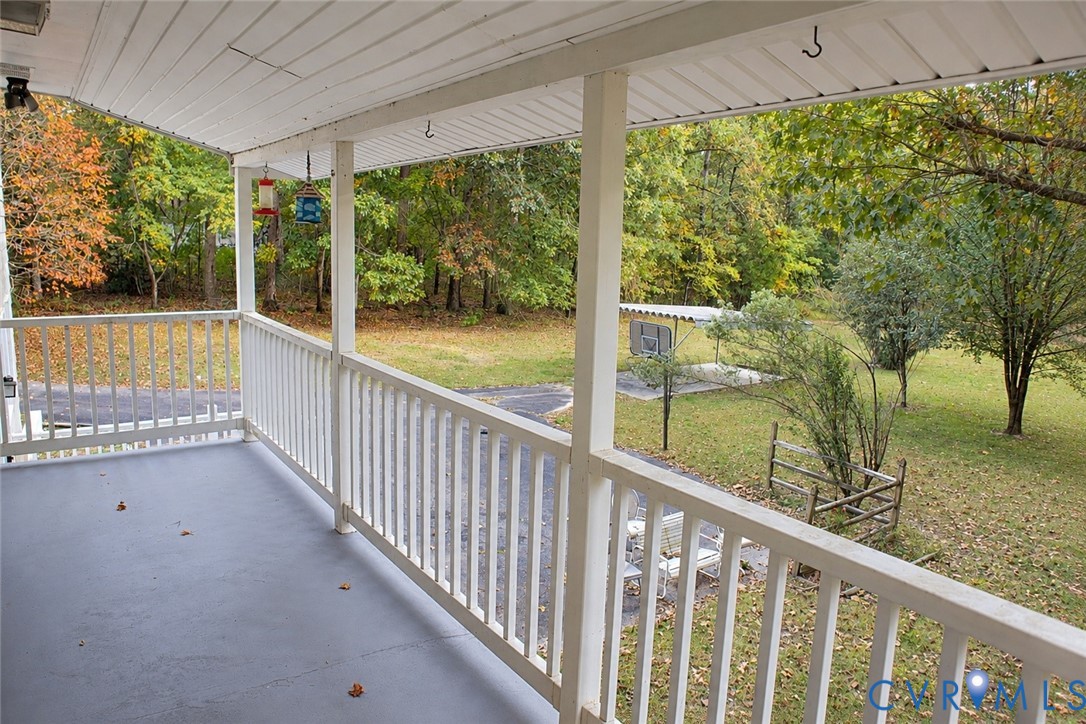 Covered porch featuring painted flooring and white structural railings, overlooking a wooded yard with mature trees Covered porch featuring painted flooring and white structural railings, overlooking a wooded yard with mature trees