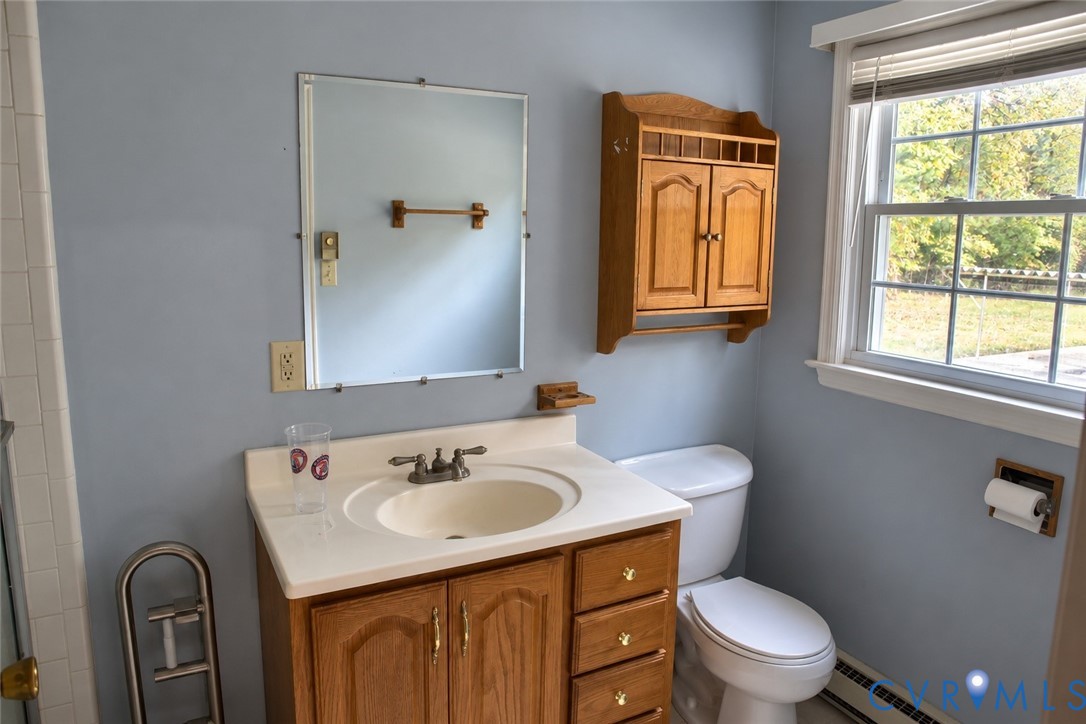 Bathroom featuring a wood vanity with integrated countertop and sink, wall-mounted wood cabinetry, a rectangular mirror, and a window with blinds Bathroom featuring a wood vanity with integrated countertop and sink, wall-mounted wood cabinetry, a rectangular mirror, and a window with blinds