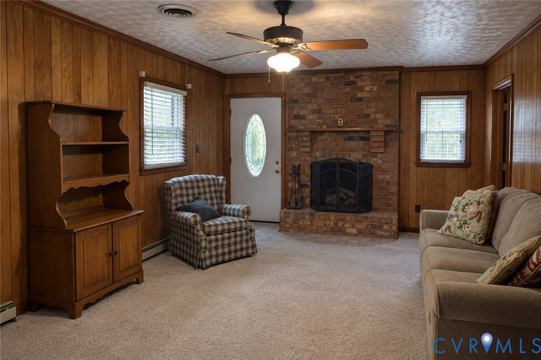 Wood-paneled walls, floor-to-ceiling brick fireplace with an integrated mantel, ceiling-mounted light fixture with fan, and solid-core entry door with an oval glass insert Wood-paneled walls, floor-to-ceiling brick fireplace with an integrated mantel, ceiling-mounted light fixture with fan, and solid-core entry door with an oval glass insert