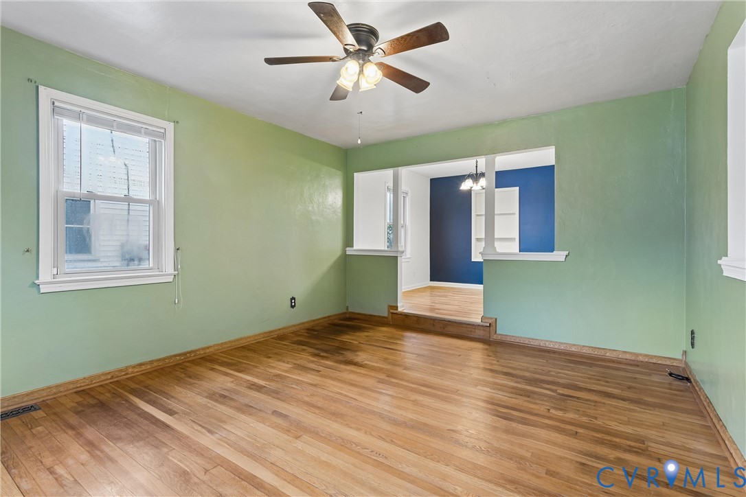 Interior room featuring wood-finish flooring, a ceiling fan with integrated lighting, multi-pane window, and a partial partition wall with a column