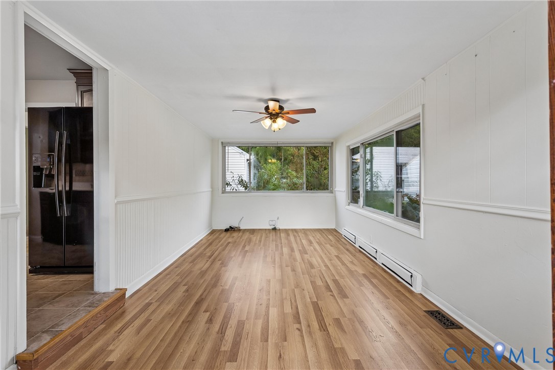 Sunroom featuring wood-finish flooring, beadboard wall paneling, a ceiling fan with integrated lighting, and large windows