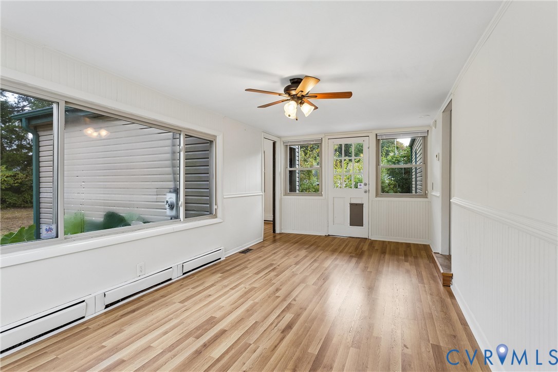 Bright interior featuring wood-finish flooring, wainscoting, a ceiling fan with integrated lighting, and a multi-pane glass entry door