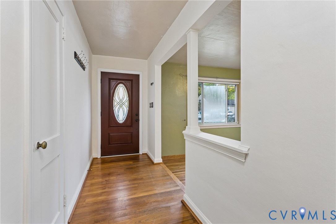 Entryway featuring wood-finish flooring, a solid core door with an oval glass insert, and a partial wall with a structural column