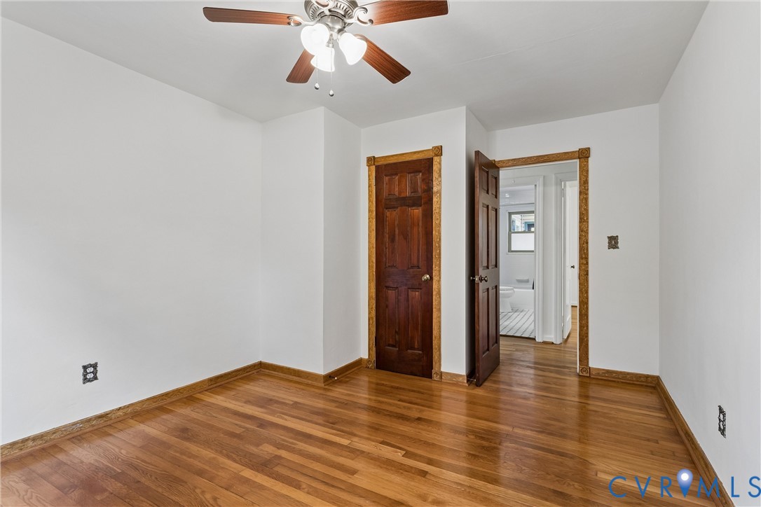 Room featuring wood-finish flooring, six-panel wood doors, stained wood trim, and a ceiling fan with integrated lighting