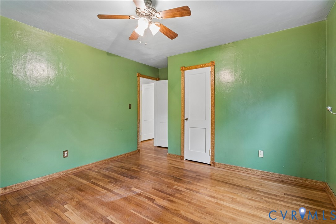 Wood-finish flooring, white paneled interior doors, decorative wood door casings, and a multi-blade ceiling fan with integrated lighting
