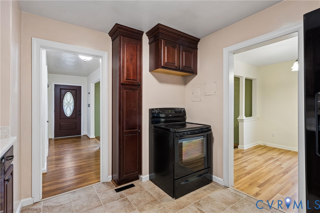 Kitchen area featuring dark wood-finish cabinetry, a freestanding black electric range, and tile flooring