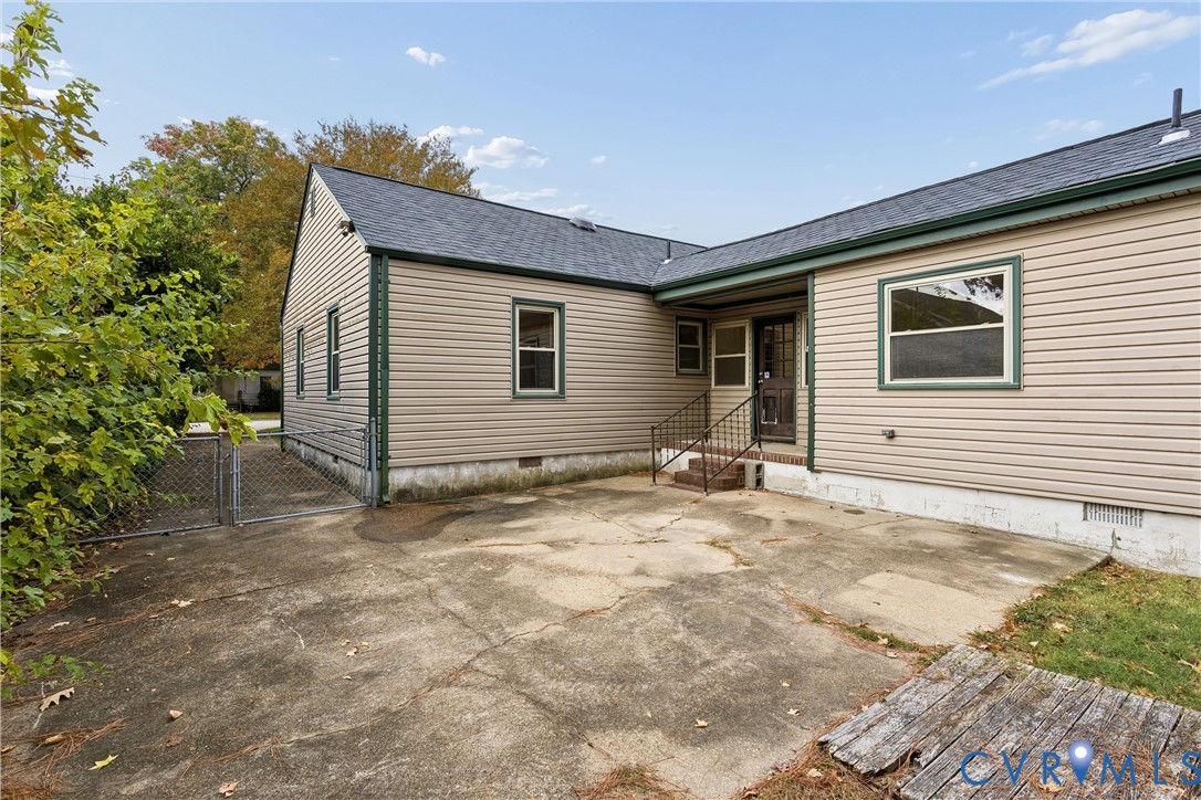 Exterior rear elevation featuring horizontal siding, a concrete patio, dark-framed windows, and metal staircase railing