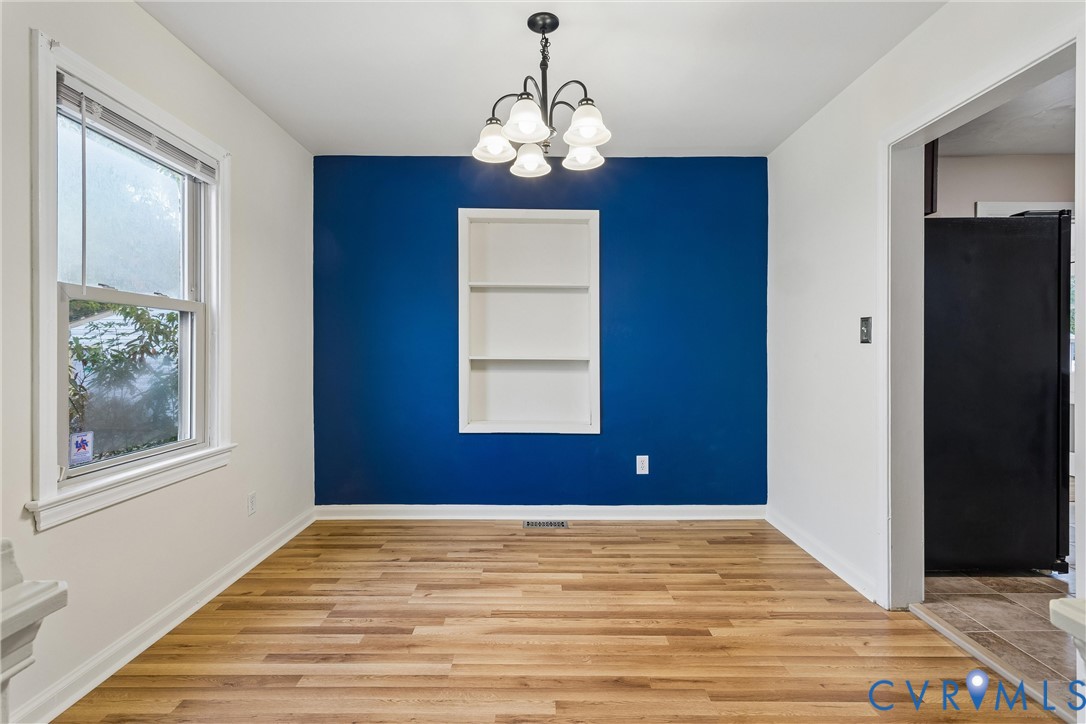 Wood-finish flooring, accent wall with built-in recessed shelving, and five-light chandelier