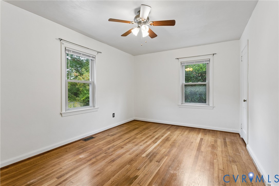 Interior room featuring wood-finish flooring, two double-hung windows, and a ceiling-mounted light fixture with a fan