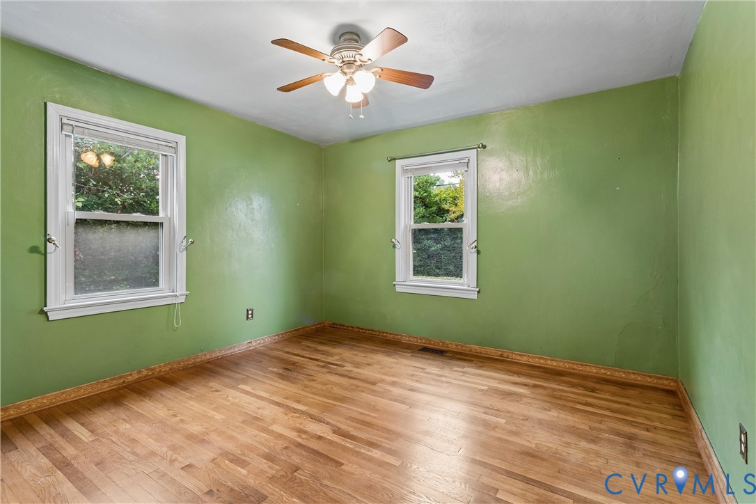 Interior room featuring wood-finish flooring, two double-hung windows with white casing, and a three-blade ceiling fan with integrated lighting