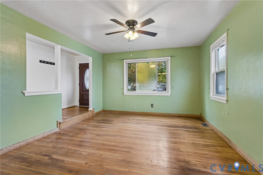 Living area featuring wood-finish flooring, a ceiling fan with integrated light fixture, multiple double-hung windows, and a built-in wall niche