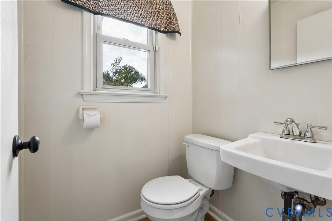 Wall-mounted mirror, white ceramic pedestal sink with polished metal faucet, and single-hung window with casing