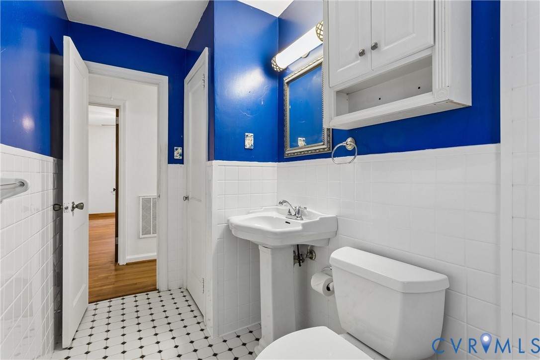White ceramic wall tile, black and white mosaic floor tile, pedestal sink, wall-mounted cabinet, and integrated lighting fixture