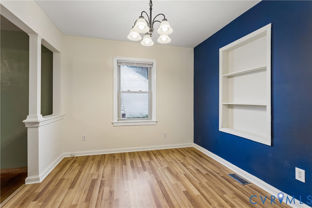 Room featuring wood-finish flooring, a built-in recessed wall shelving unit, a five-light chandelier, and a partial wall divider with a column