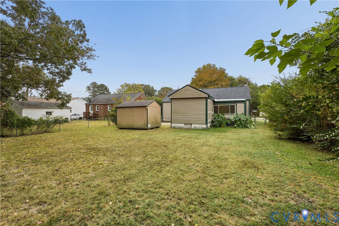 Expansive backyard featuring a level lawn, mature perimeter trees, a detached storage shed, and vinyl siding exterior finishes