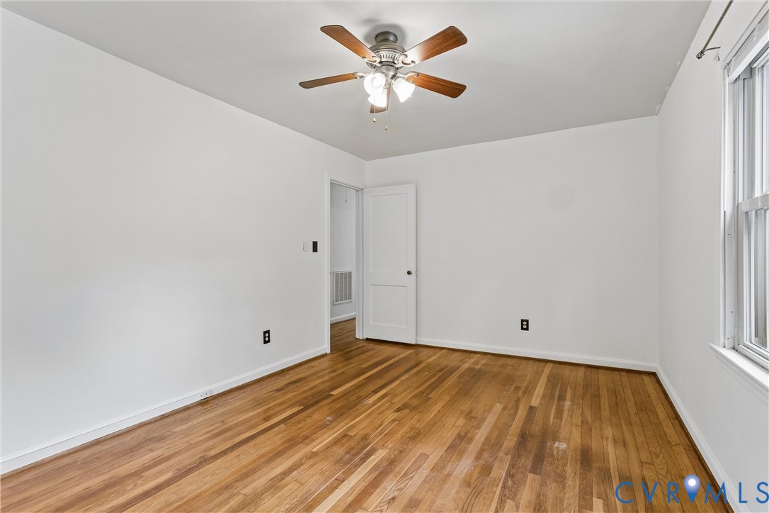 Room featuring wood-finish flooring, a multi-blade ceiling fan with integrated lighting, and a paneled interior door