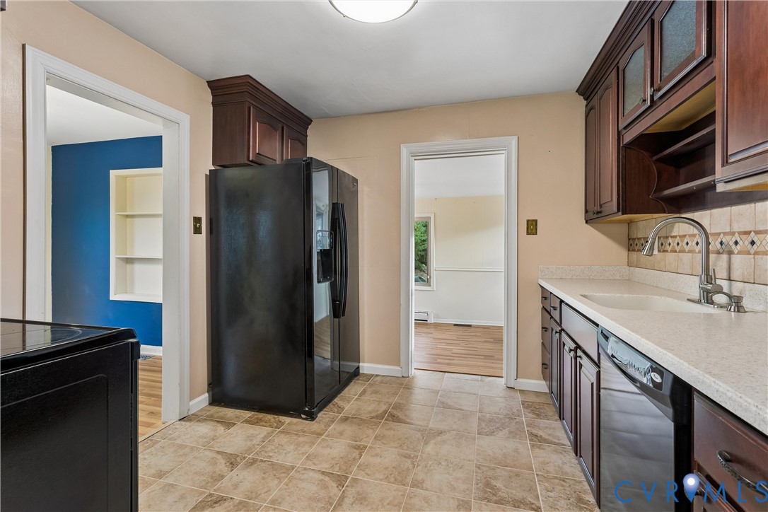 Kitchen featuring dark wood cabinetry, light stone-finish countertops, tiled backsplash, integrated sink with gooseneck faucet, and tile flooring