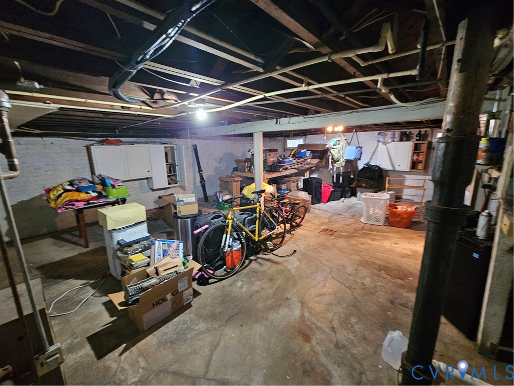 Unfinished lower level featuring concrete flooring, exposed ceiling joists, painted masonry walls, and built-in wall cabinetry