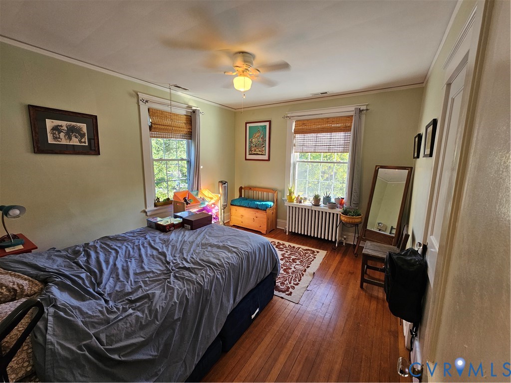 Wood-finish flooring, two sash windows with natural light, a ceiling-mounted light fixture, and a metal radiator