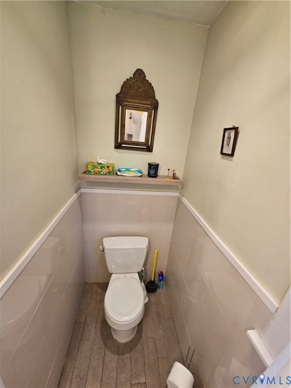 Half-bath featuring wood-finish flooring, ceramic tile wainscoting, and a built-in wall shelf