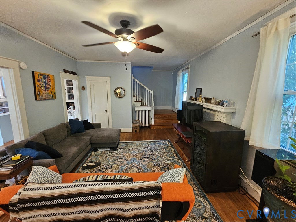 Living area featuring wood-finish flooring, a ceiling fan with integrated lighting, a fireplace mantle, and staircase with white millwork railings