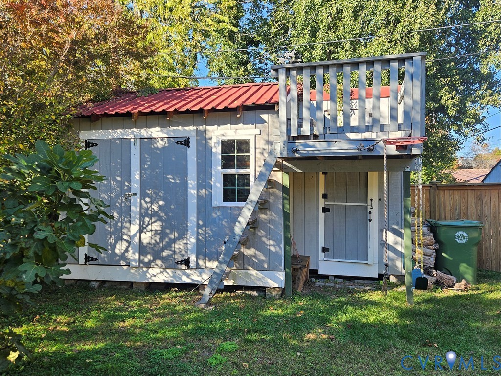 Outbuilding with a red metal roof, vertical board-and-batten siding, double entry doors, single-hung window, and an attached elevated wooden deck with a ladder
