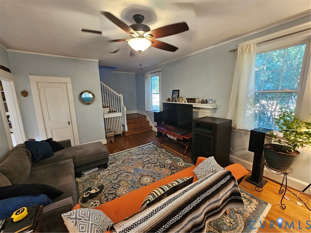 Living area featuring wood-finish flooring, a ceiling fan with integrated lighting, multi-pane windows, and a classic fireplace mantel
