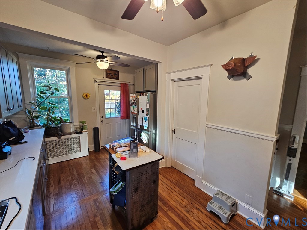Kitchen area featuring wood-finish flooring, white solid-surface countertops, wainscoting, dual ceiling fans, and a glass-paneled exterior door