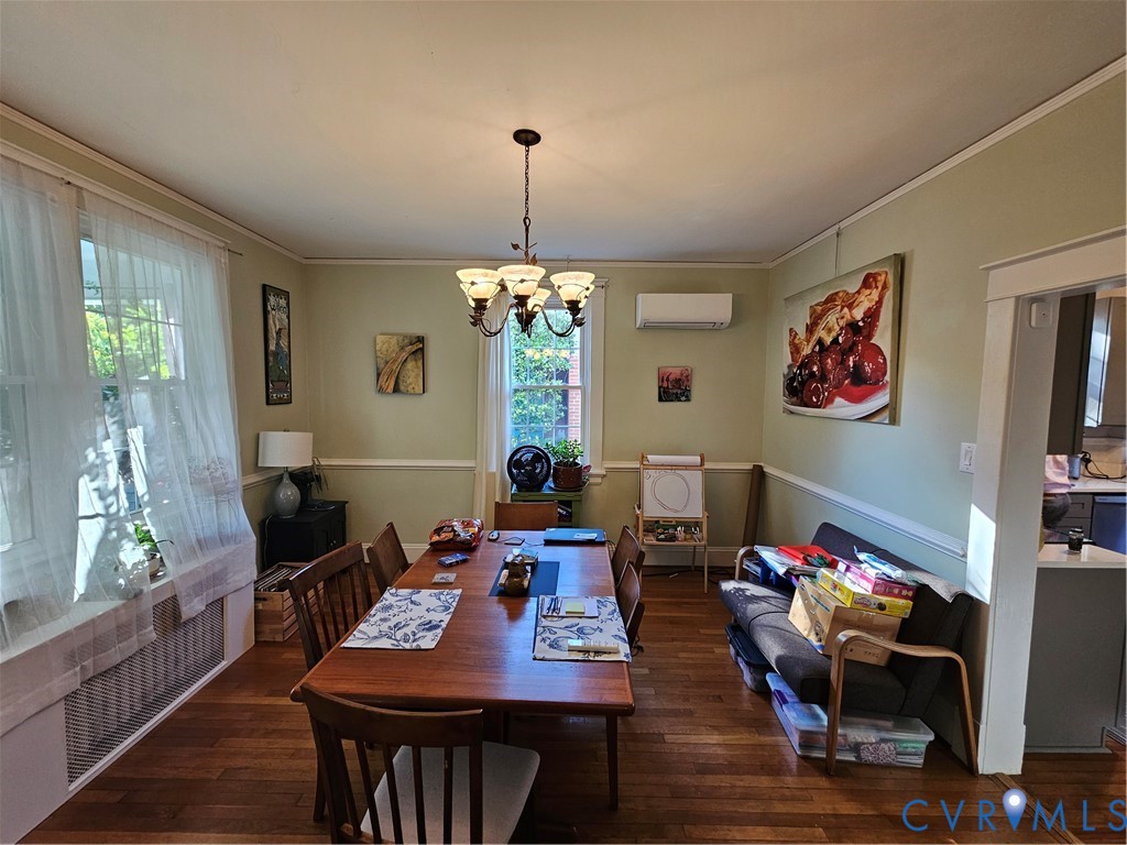 Dining area featuring wood-finish flooring, chair rail molding, a multi-light chandelier, and a wall-mounted ductless climate control unit