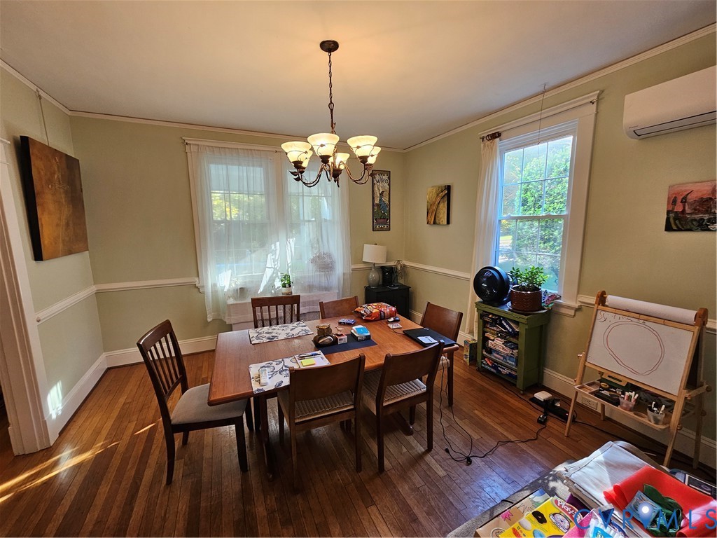 Dining area featuring wood-finish flooring, crown molding, chair rail trim, a multi-arm chandelier, and a wall-mounted mini-split system