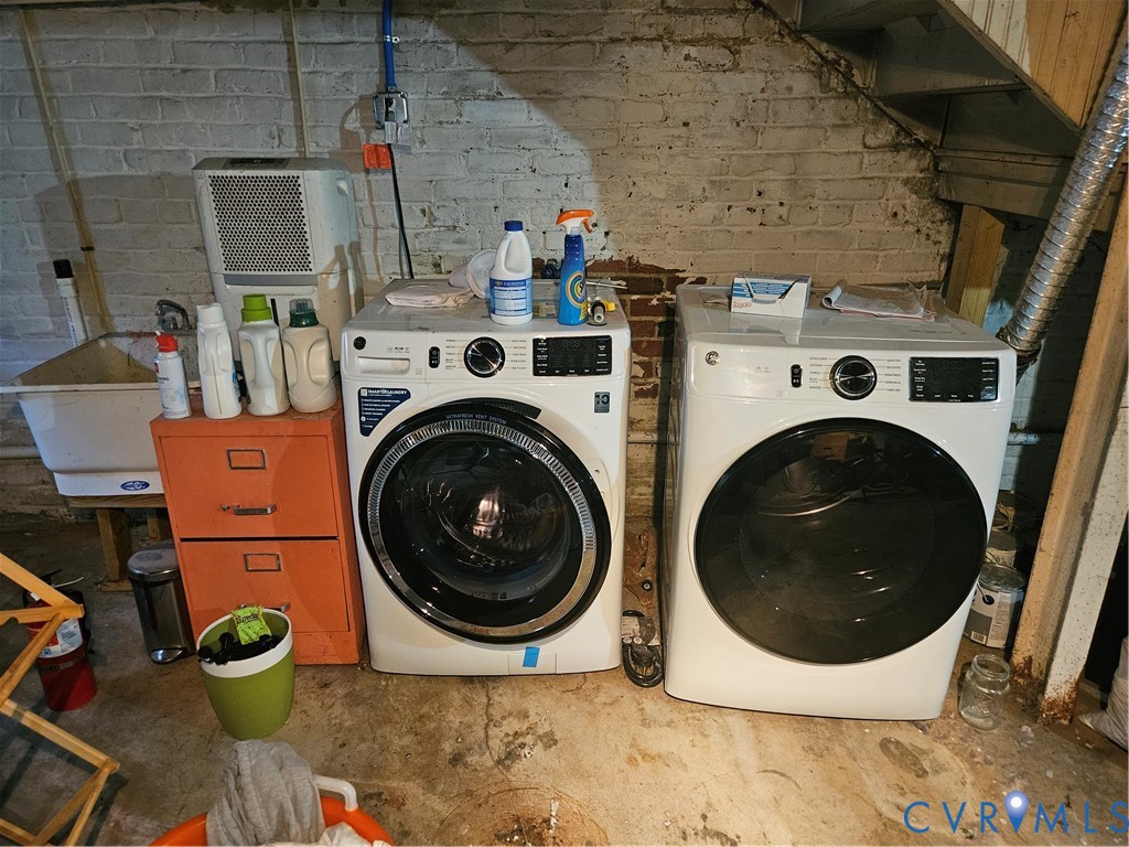 Laundry area featuring a front-load washer and dryer set, white utility sink, and painted brick masonry walls