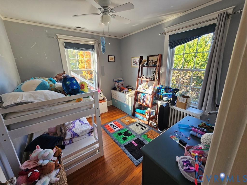 Room featuring hardwood flooring, two double-hung windows with exterior trim, and a ceiling-mounted light fixture with fan