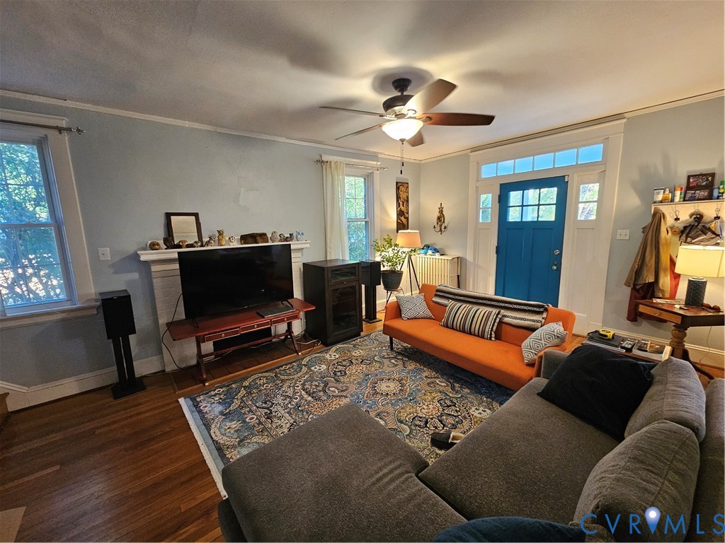 Hardwood flooring, wood-burning fireplace with mantel, ceiling fan, and entry door with transom window