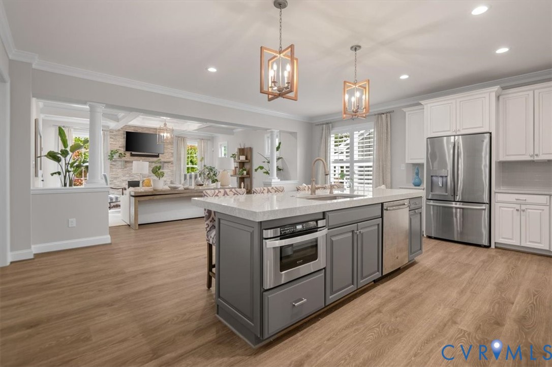 Kitchen featuring wood-finish flooring, a central island with quartz countertops, custom two-toned cabinetry, stainless steel appliances, and geometric pendant lighting