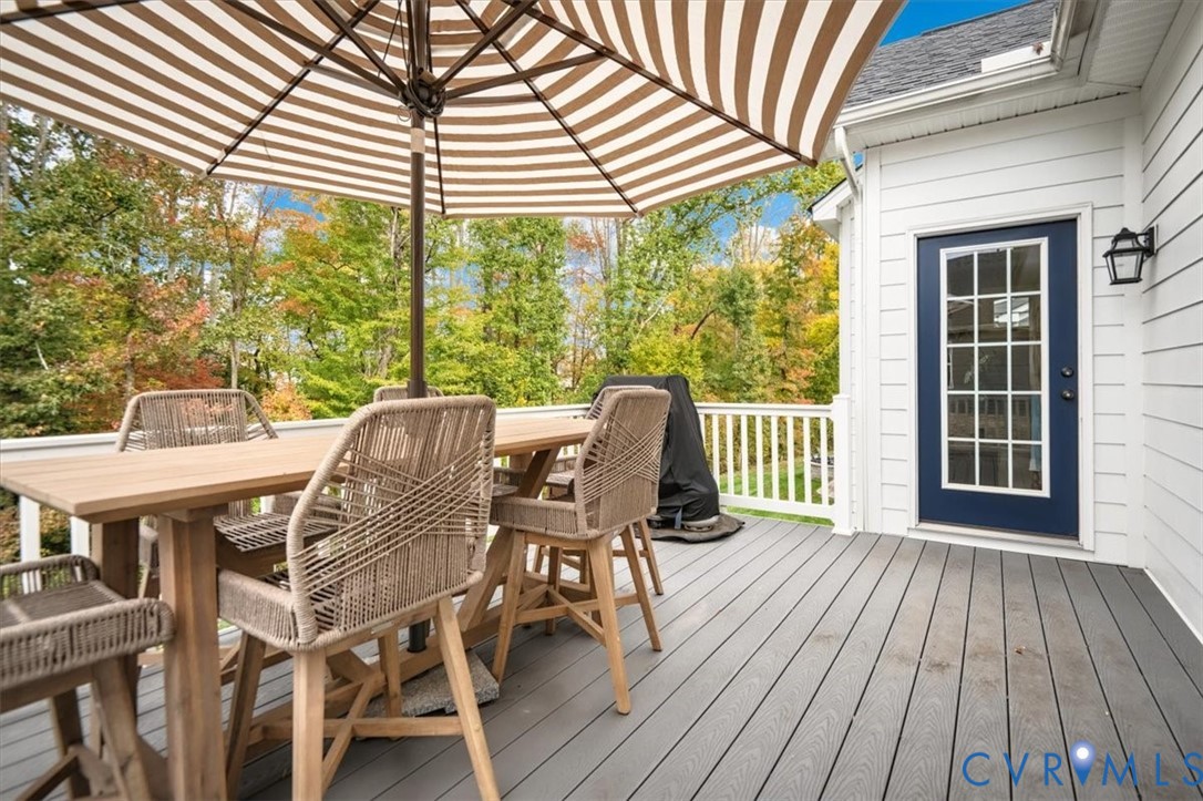Elevated deck featuring gray composite decking, white baluster railings, horizontal lap siding, and a multi-pane glass entry door