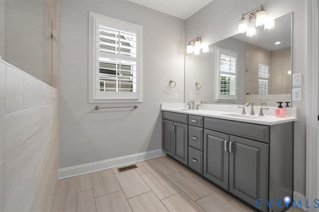 Double vanity featuring a white surface, charcoal-grey shaker cabinetry, dual under-mount sinks, polished chrome fixtures, and a large wall-mounted mirror