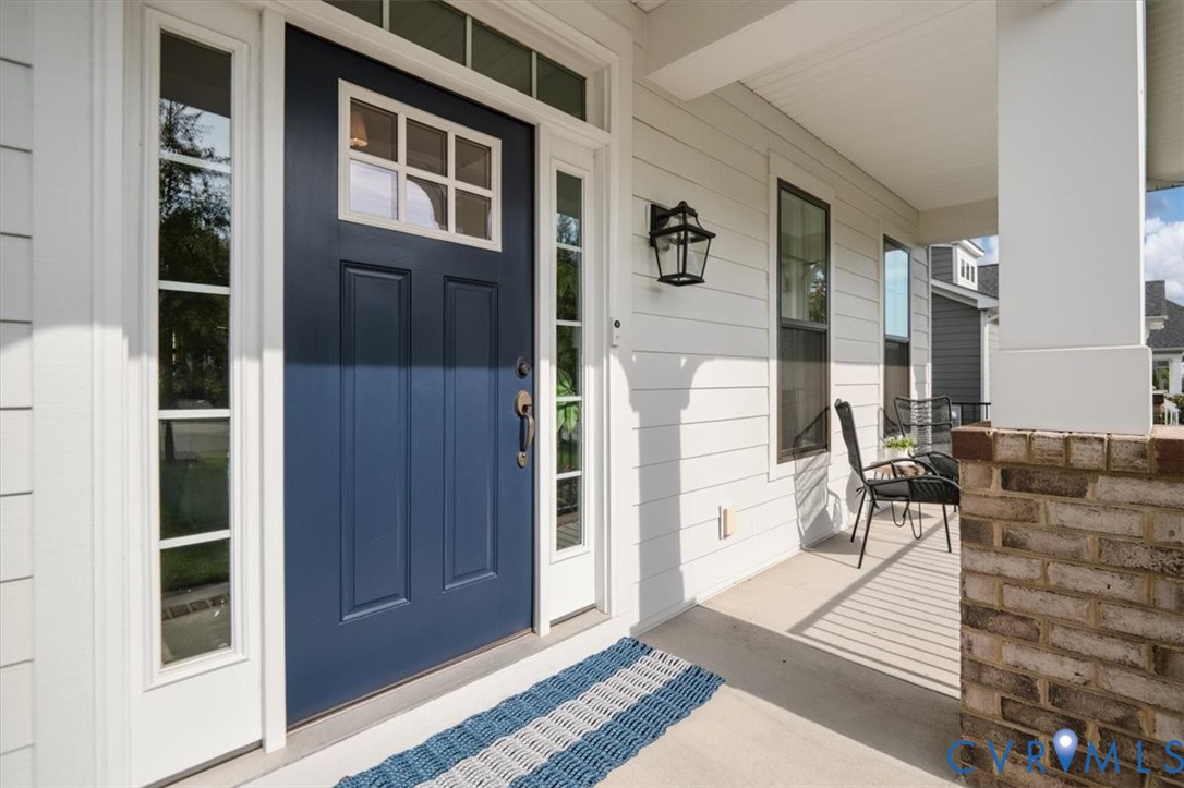 Covered entryway featuring a navy blue front door with a transom window, sidelights, exterior sconce lighting, and a brick-based support column