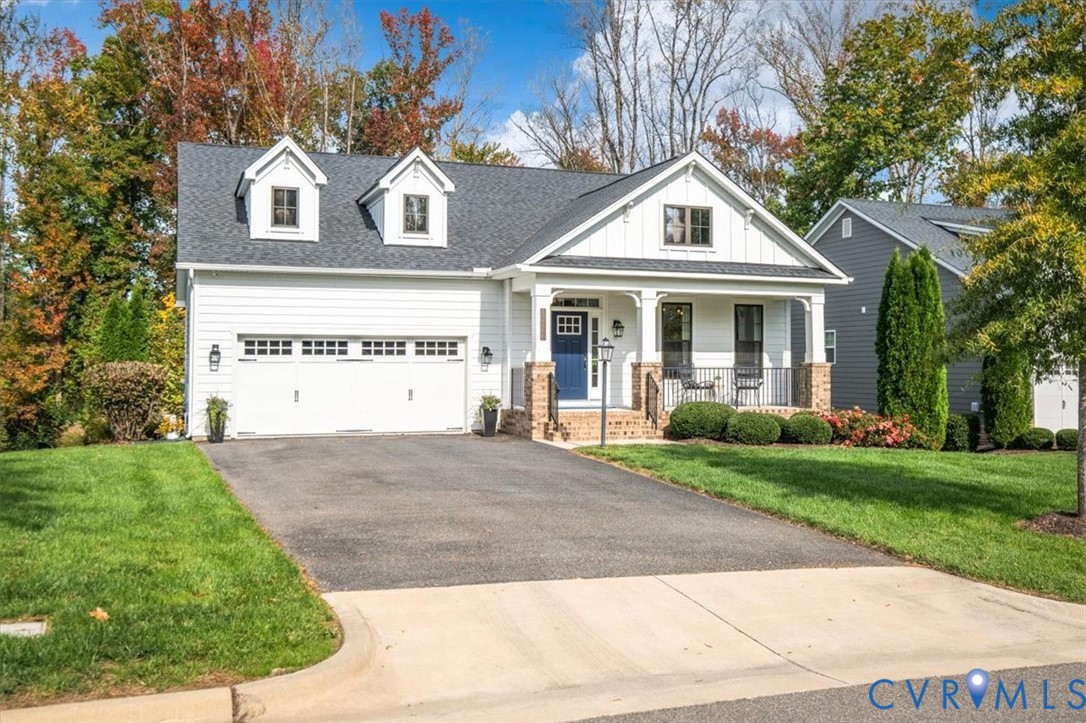 Two-story residence featuring white horizontal siding, a covered front porch with brick column bases, a two-car garage, and dual roof dormers
