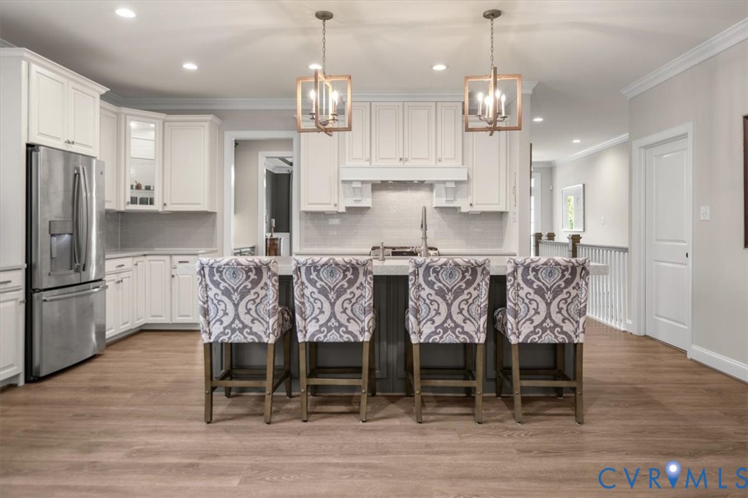 Kitchen featuring shaker-style cabinetry, stainless steel refrigerator, stone-surface central island, and wood-finish flooring, accented by geometric pendant lighting