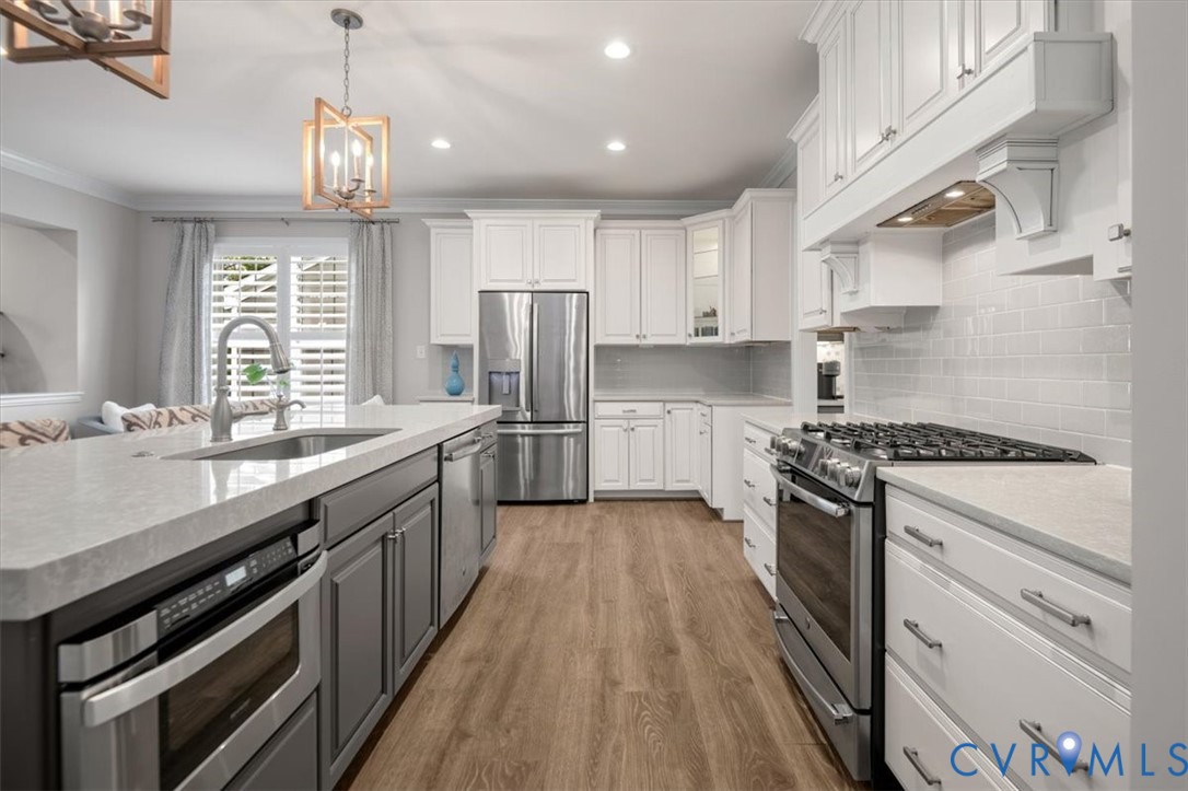 Kitchen featuring white shaker cabinetry, stainless steel appliances, stone-surface countertops, subway tile backsplash, and wood-finish flooring