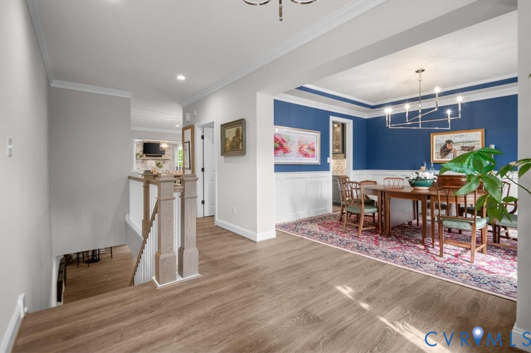 Wood-finish flooring, white wainscoting, multi-arm chandelier, and a wood-post staircase railing
