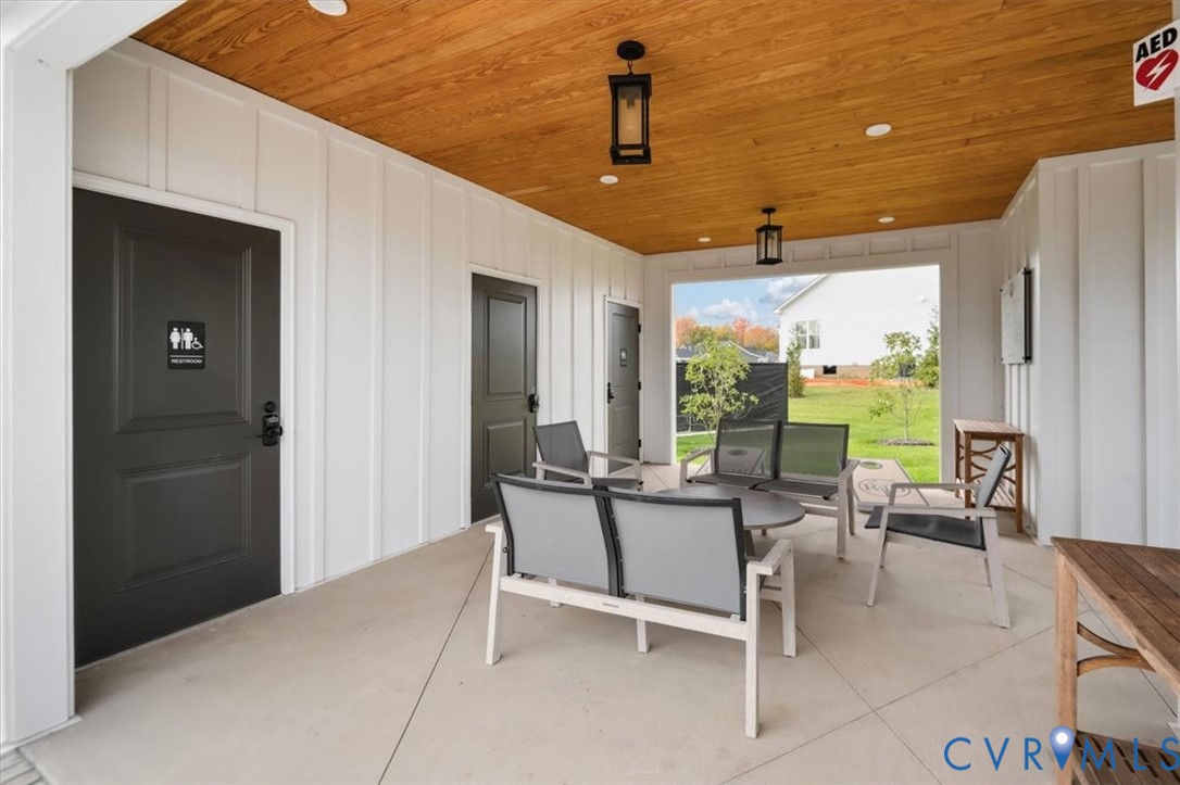Covered patio featuring a wood-plank ceiling, board-and-batten siding, concrete flooring, and matte black pendant lighting