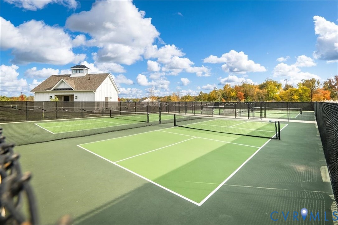 Multiple outdoor courts featuring synthetic surface material and black chain-link fencing, accompanied by a detached structure with a cupola and white siding