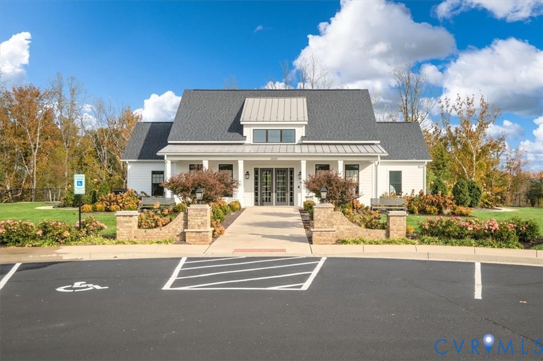 Single-story exterior featuring a metal-accented roof, symmetrical gable design, covered front porch, masonry piers, and concrete walkway