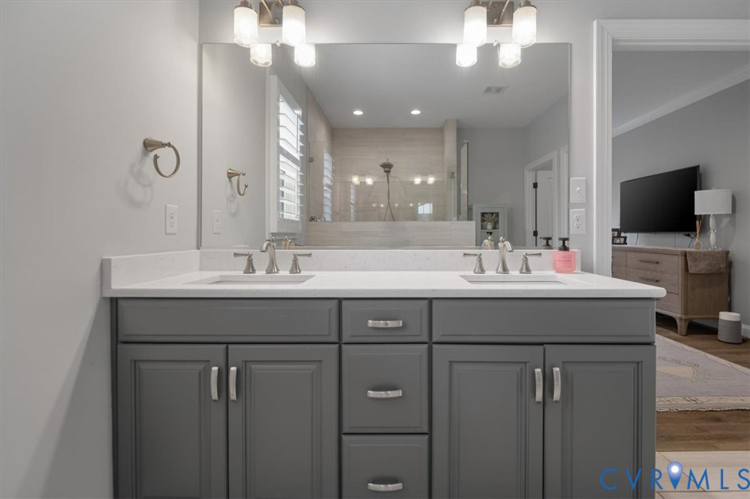 Dual-sink vanity with a solid-surface countertop, cabinetry in a grey finish, brushed nickel hardware, and dual-bulb wall-mounted lighting fixtures